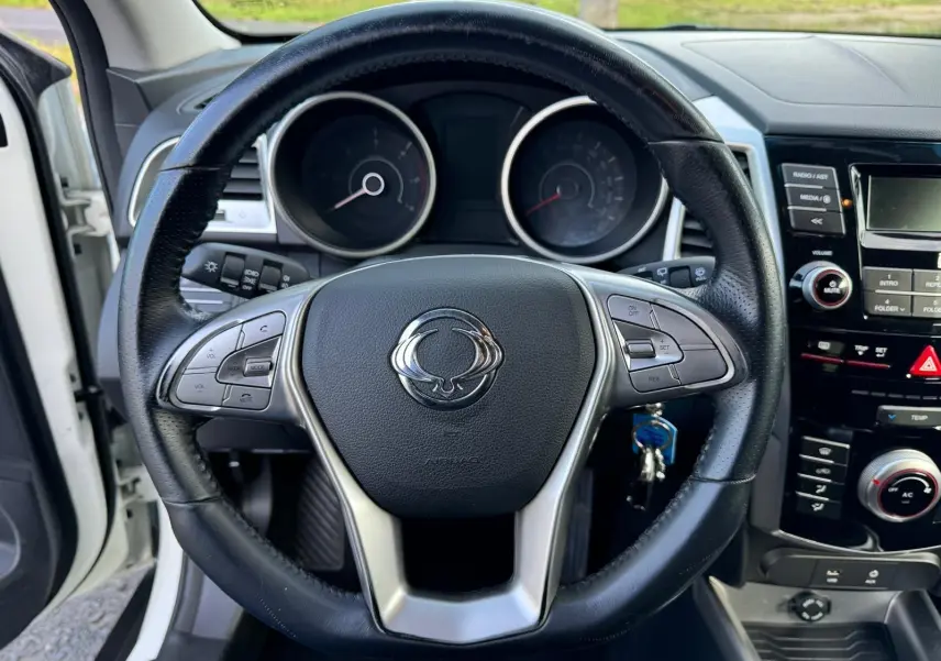 Vue rapprochée du volant en cuir noir du SsangYong Tivoli blanc 2016, avec commandes intégrées et tableau de bord visible.