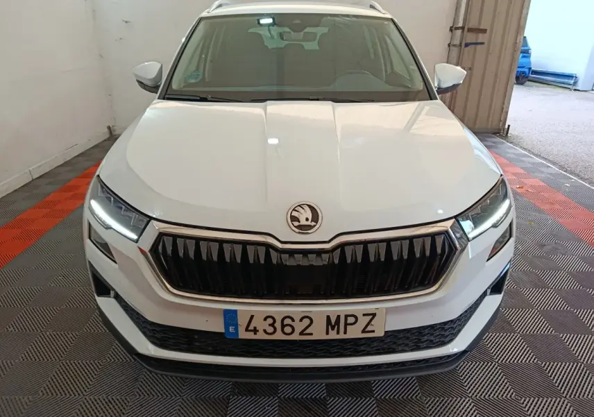 Vue avant d'un Skoda Karoq blanc 2024 avec calandre noire et phares LED allumés dans un garage.