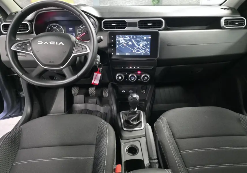 Vue intérieure avant du Dacia Duster 2024, tableau de bord noir avec écran tactile et volant multifonction.