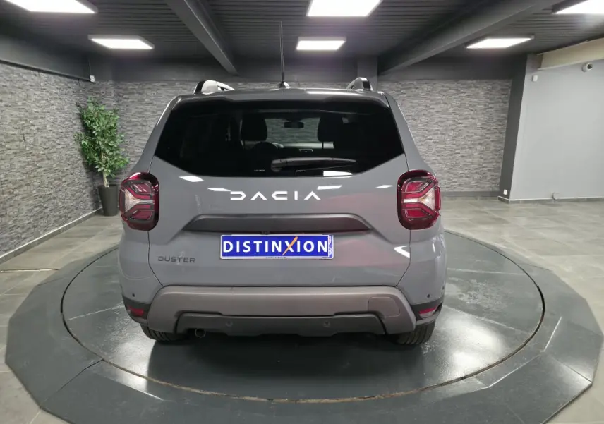 Vue arrière d'un Dacia Duster gris urbain avec logo blanc et feux arrière au design carré, en showroom.
