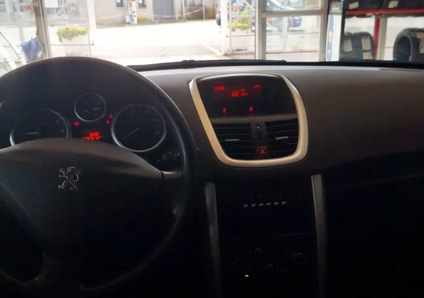 Intérieur de la Peugeot 207+ 2013 montrant le tableau de bord et le volant noir avec affichage numérique rouge.