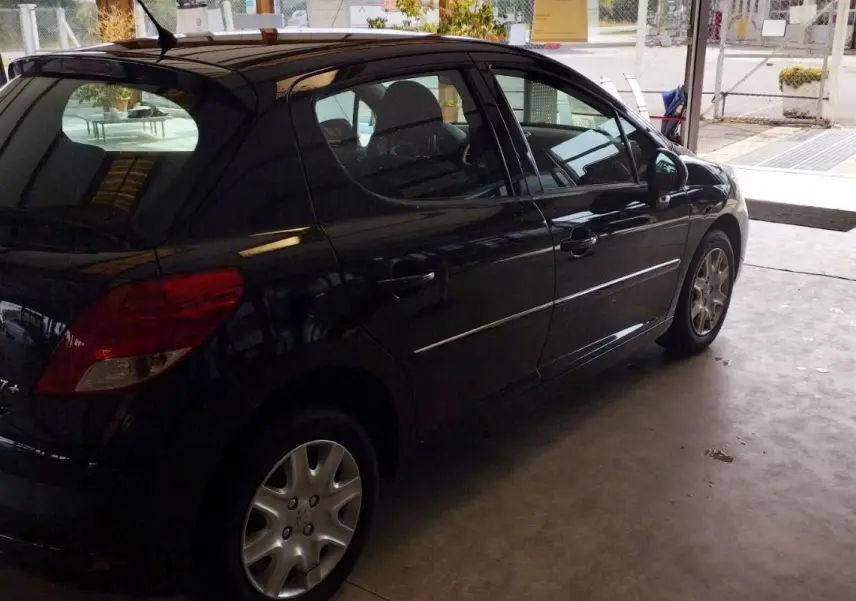 Peugeot 207+ noire vue de trois quarts arrière côté droit, stationnée dans un garage lumineux.