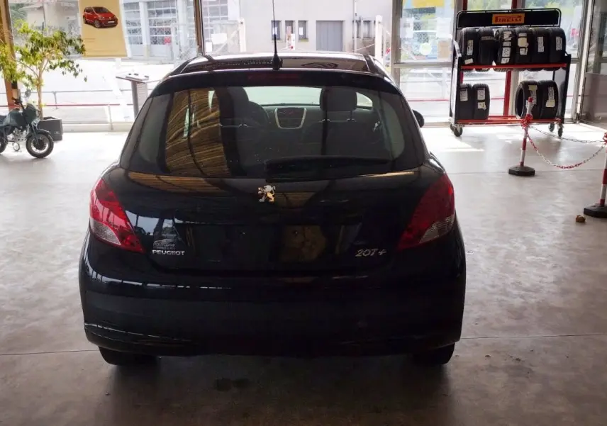 Vue arrière d'une Peugeot 207+ noire de 2013, avec logo et badges visibles dans un garage lumineux.