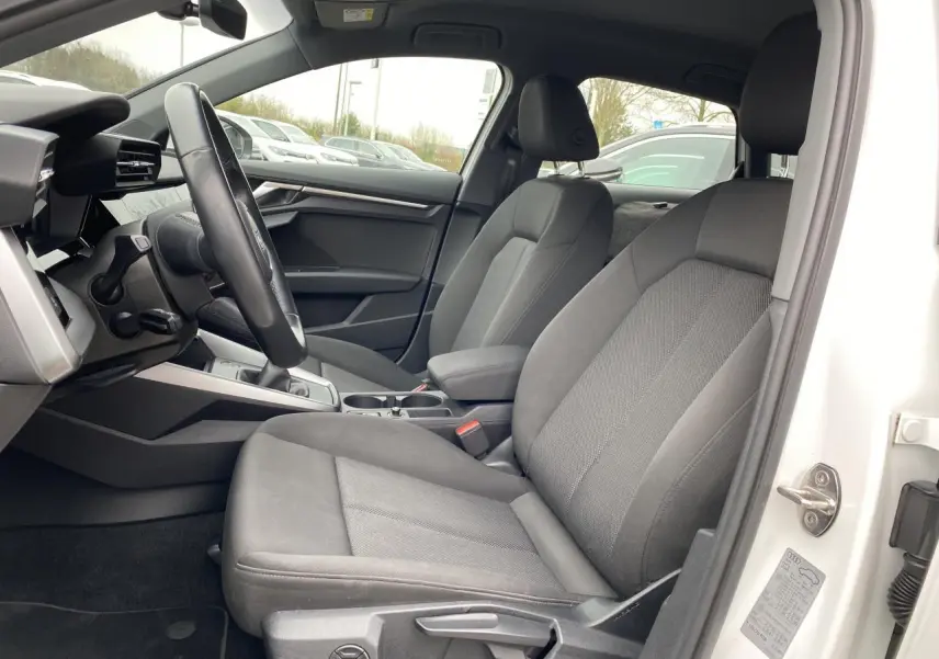 Vue intérieure côté conducteur de l'Audi A3 Sportback blanc Ibis 2022 avec sièges tissu gris et volant cuir.