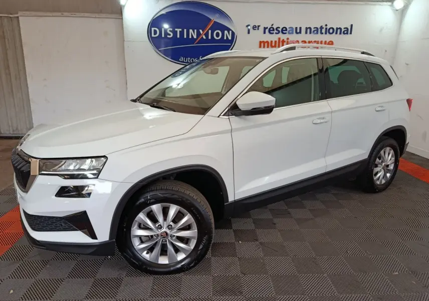 SKODA KAROQ blanc vue 3/4 avant droit en intérieur avec jantes argentées et barres de toit noires.