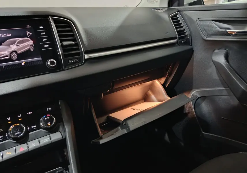 Intérieur de la Skoda Karoq 2024, vue côté passager sur la boîte à gants ouverte avec éclairage intérieur et écran tactile central.