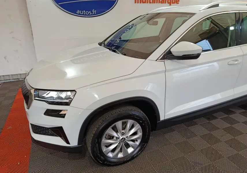 Vue 3/4 avant gauche d'un SKODA KAROQ blanc 2024 avec phares LED et jantes alliage argentées.