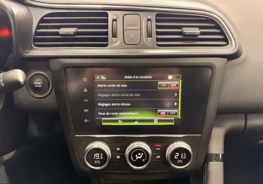 Vue rapprochée du tableau de bord du Renault Kadjar blanc, affichant l'écran tactile des aides à la conduite et les commandes de climatisation.