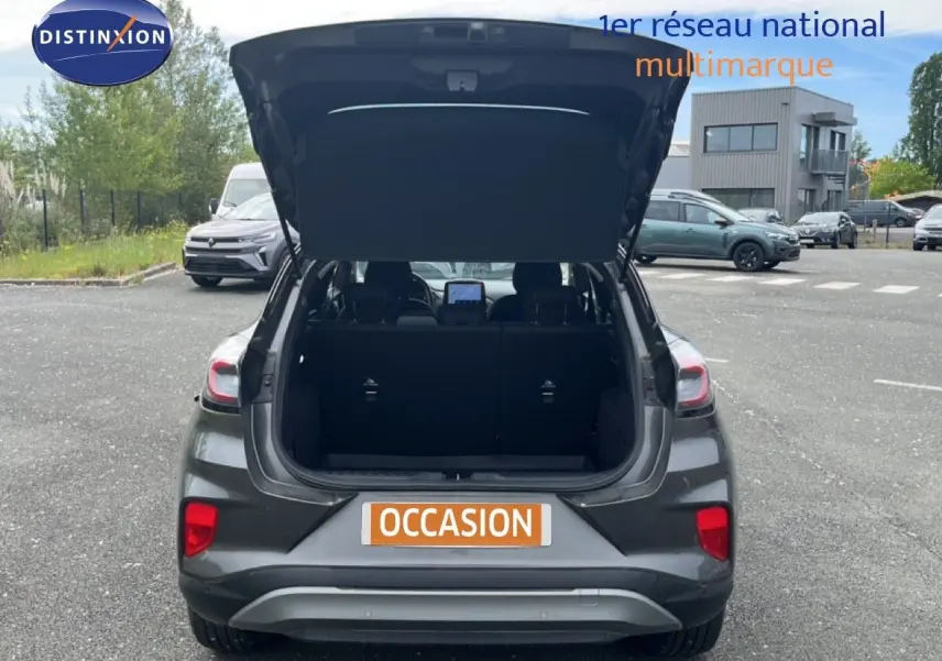 Vue arrière d’un Ford Puma gris 2021 avec coffre ouvert, mettant en valeur l’espace de chargement et les feux arrière.