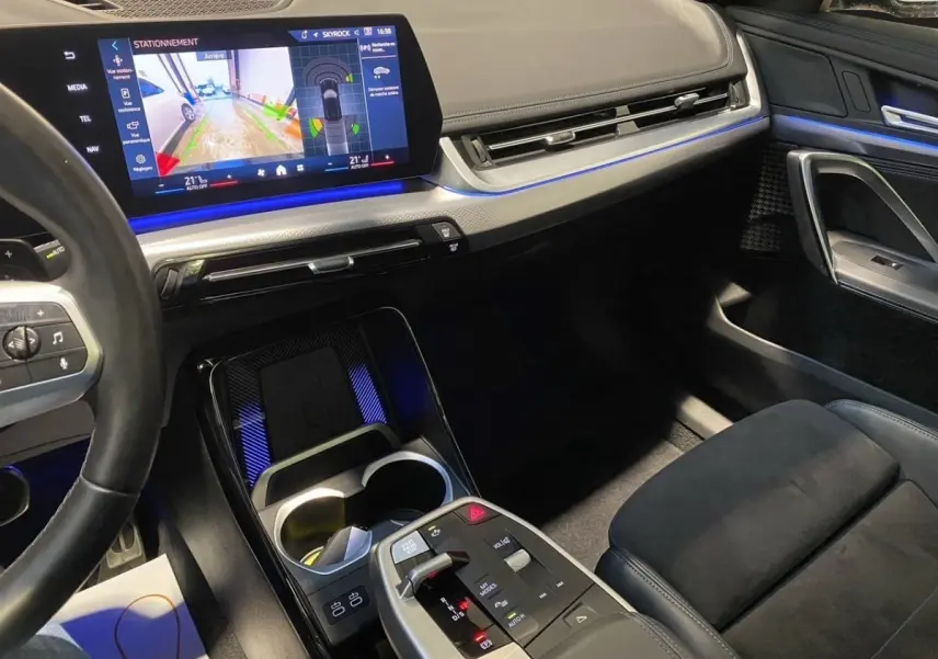 Vue intérieure côté passager du tableau de bord et console centrale du BMW X1 noir avec écran tactile et éclairage d’ambiance bleu.