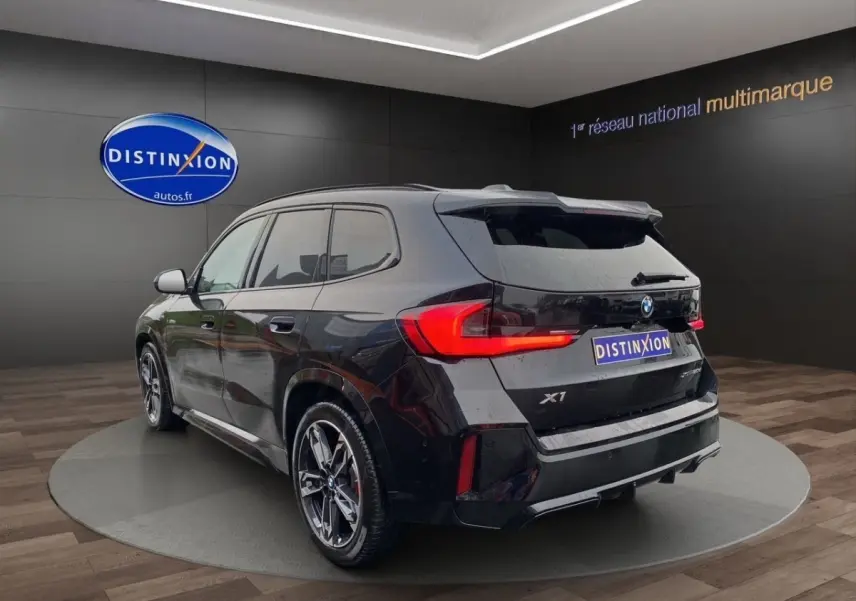 BMW X1 noir en 3/4 arrière droit, avec feux LED distinctifs et jantes sport M visibles en showroom.