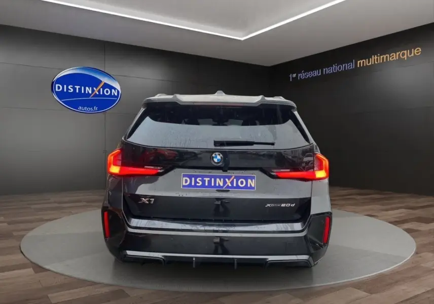 Vue arrière d'un BMW X1 noir xDrive20d avec feux LED caractéristiques et logo distinctif sur fond showroom.