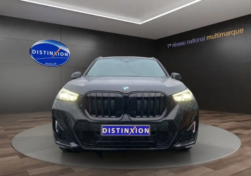 Vue frontale d’un BMW X1 noir avec calandre noire et phares allumés dans un showroom.