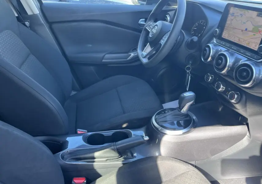 Intérieur avant du Nissan Juke 2023 vu côté conducteur, sièges tissu noir et écran tactile GPS visible.