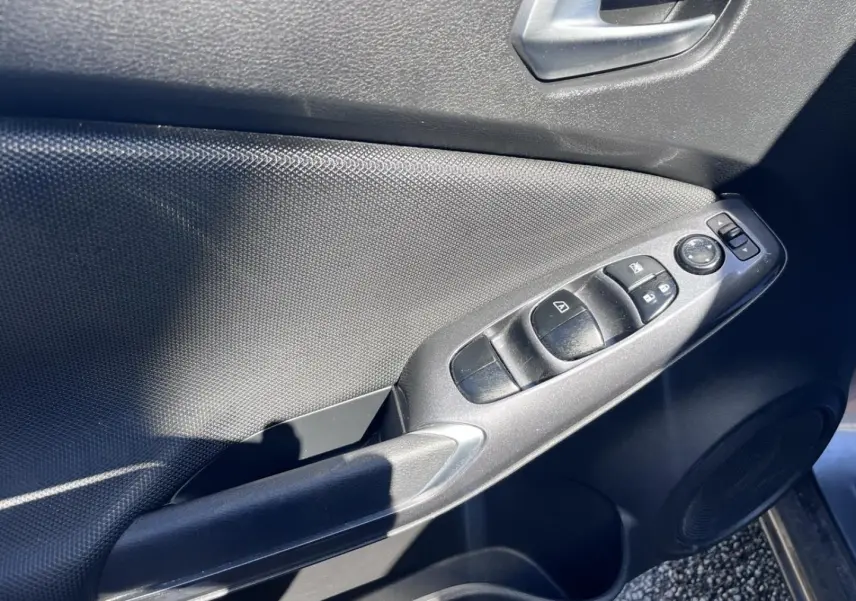 Panneau de porte côté conducteur du Nissan Juke 2023 gris, avec commandes électriques des vitres et rétroviseurs.