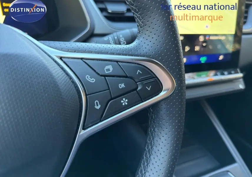 Gros plan sur la partie gauche du volant en cuir perforé noir du Renault Symbioz 2025, avec commandes intégrées et écran tactile flou en arrière-plan.