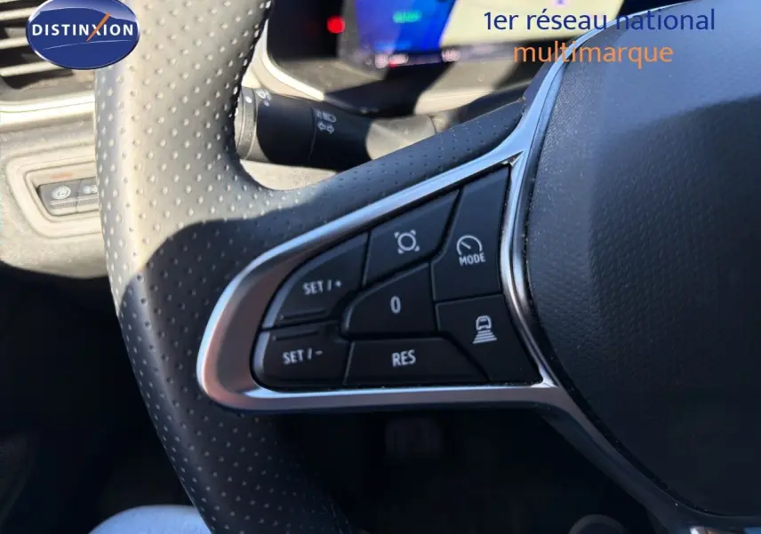 Gros plan sur les commandes au volant perforé du Renault Symbioz gris Rafale, mettant en valeur les boutons de régulateur et mode de conduite.