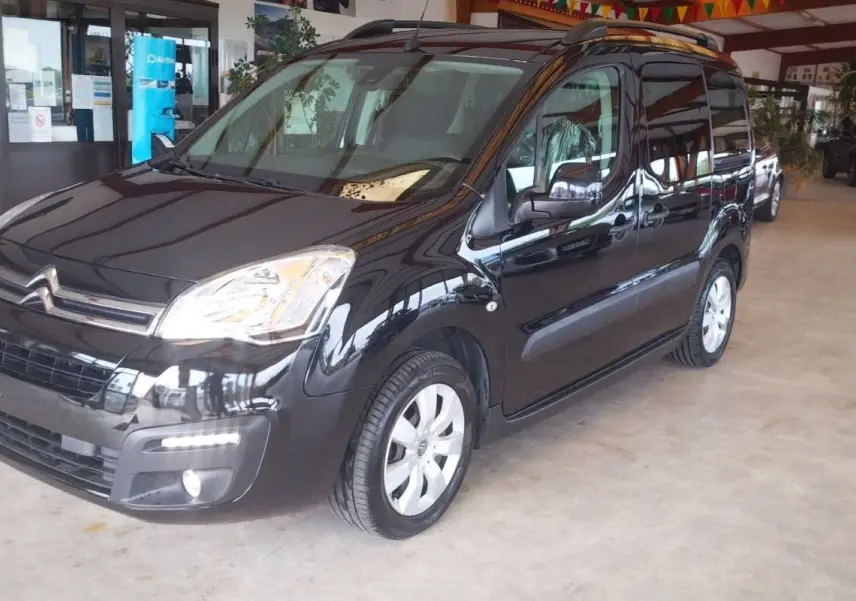 Citroën Berlingo noir en 3/4 avant droit, montrant ses phares et la calandre dans un showroom intérieur.