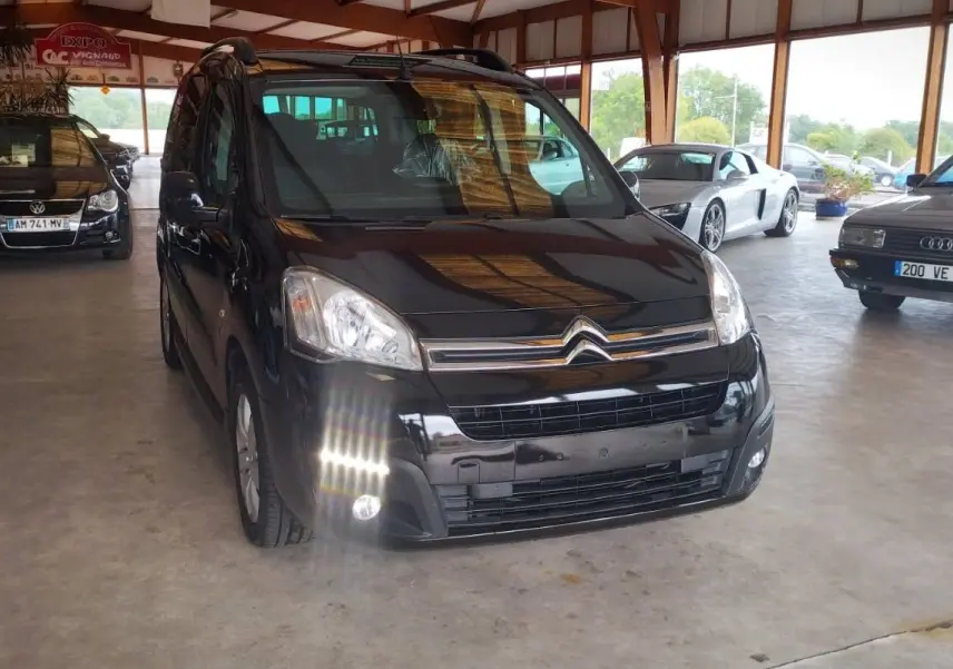 Vue 3/4 avant d'un Citroën Berlingo noir 2016, avec phares allumés, dans un showroom lumineux.