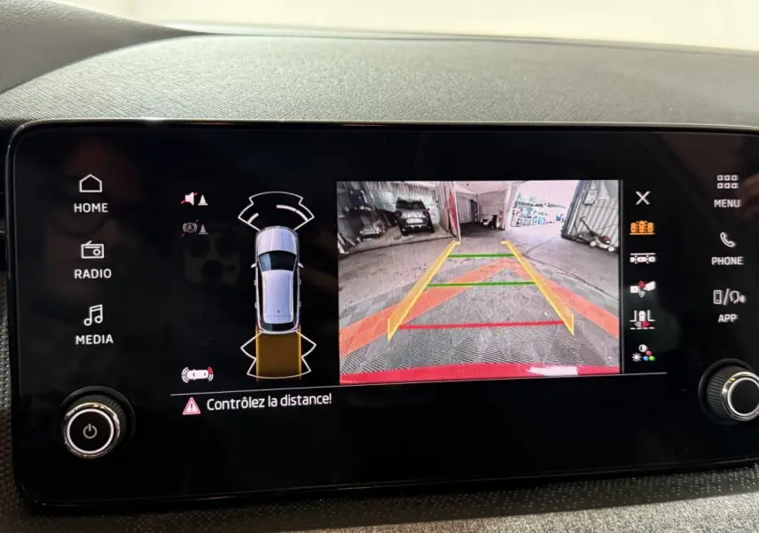 Écran tactile central du Skoda Kamiq rouge 2024 montrant la caméra de recul avec aides au stationnement.