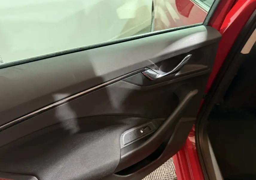 Vue rapprochée de la porte avant gauche rouge d’un Skoda Kamiq 2024 avec poignée chromée et commande de vitre électrique.