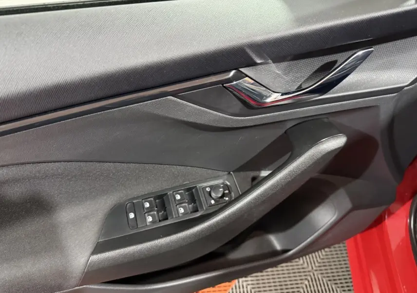 Détail de la porte côté conducteur d’une Skoda Kamiq rouge, montrant les commandes des vitres et rétroviseurs.
