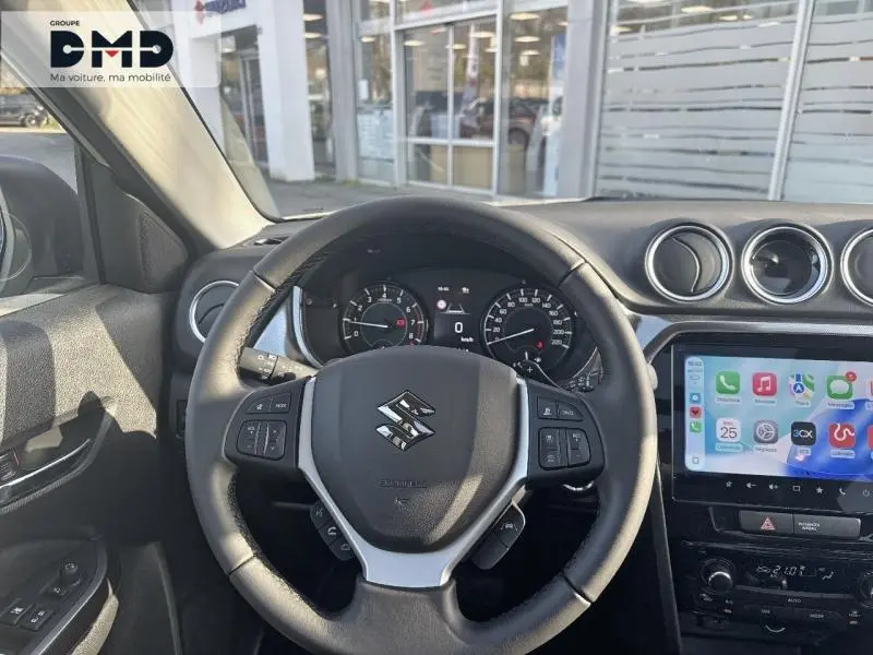 Vue intérieure frontale du volant cuir noir multifonction du Suzuki Vitara 1.4 Boosterjet Hybrid avec écran tactile et tableau de bord digital.
