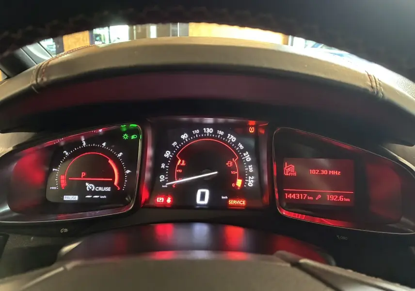 Vue rapprochée du tableau de bord numérique rougeoyant de la DS5 gris, affichant vitesse, compte-tours et radio FM.