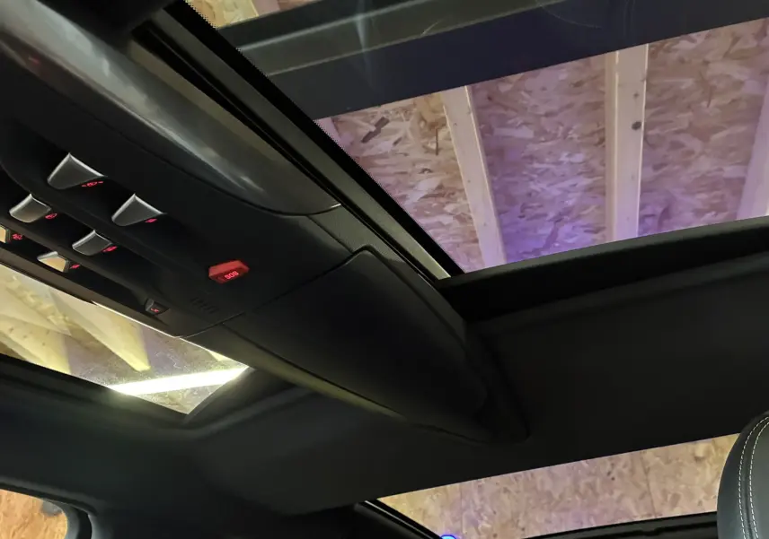 Vue intérieure du toit ouvrant panoramique et des commandes au plafond d'une DS5 gris 2018, ambiance sombre.