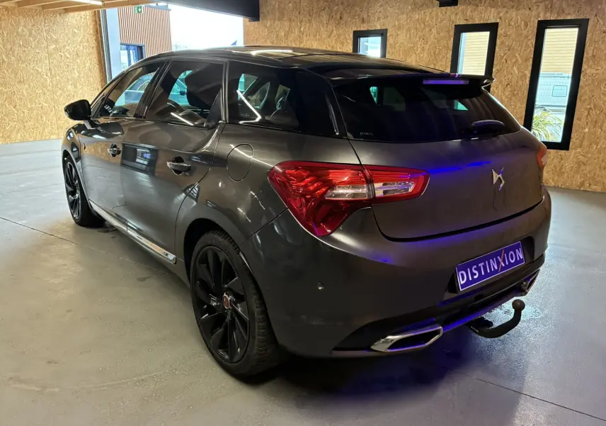 Vue 3/4 arrière droite d'une DS5 gris métallisé 2018 avec jantes noires et attelage dans un garage.