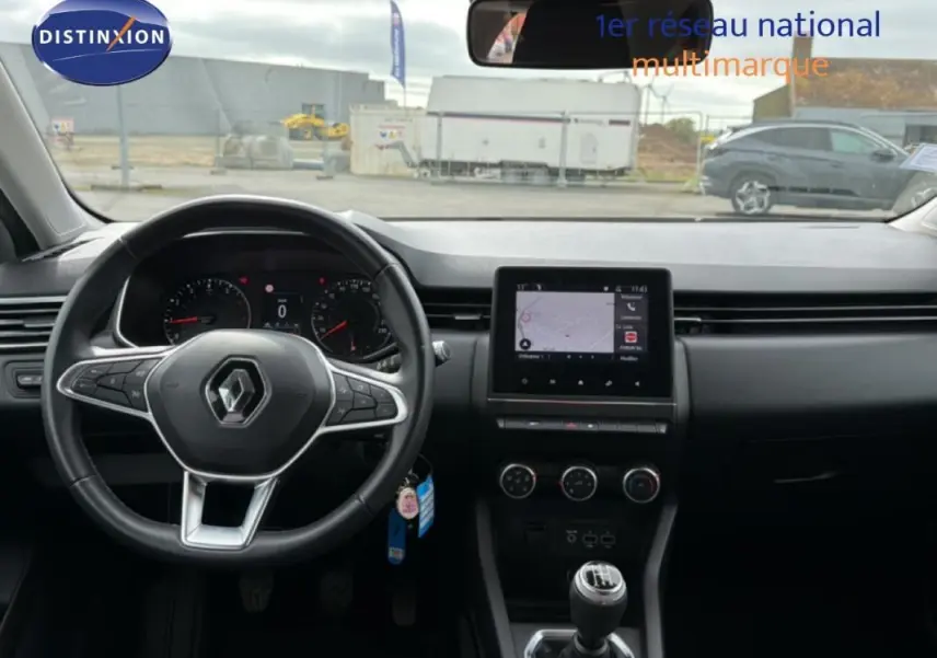 Vue intérieure frontale du tableau de bord et volant noir d'une Renault Clio blanche, avec écran tactile et boîte manuelle.