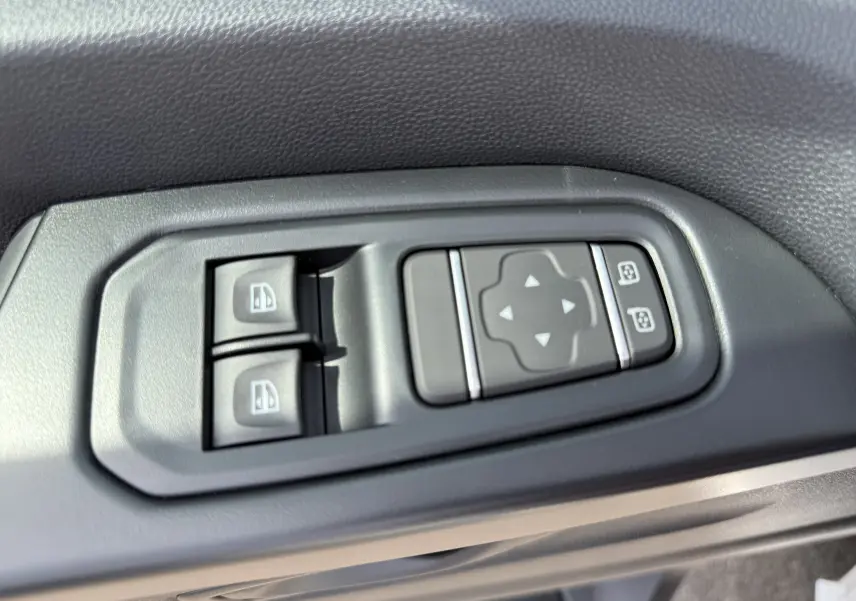 Gros plan sur les commandes de réglage des rétroviseurs et des vitres électriques côté conducteur du Renault Trafic Fourgon blanc.