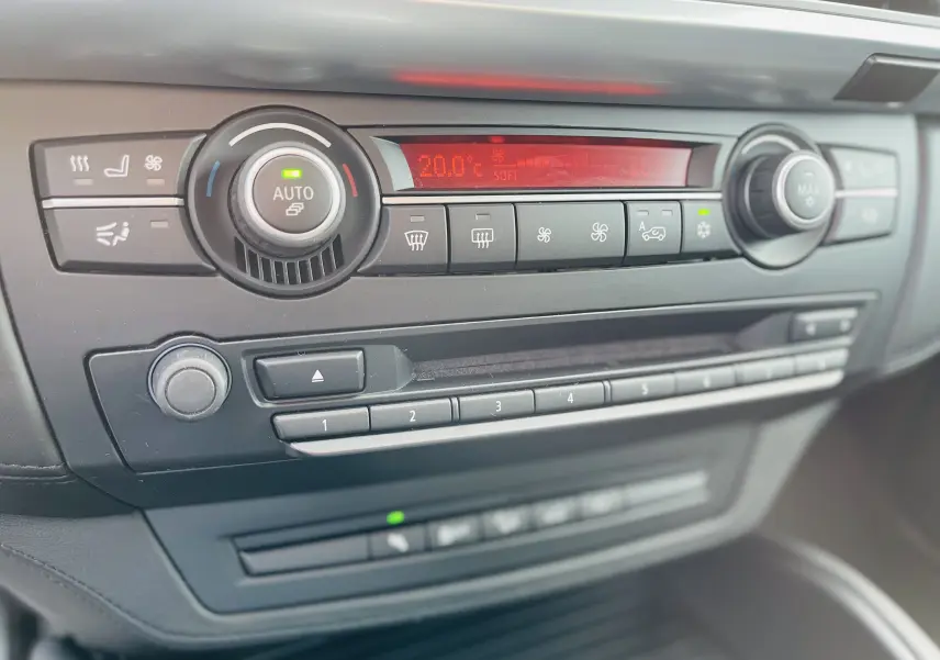 Gros plan sur la console centrale noire du BMW X6 50D, affichant les commandes de climatisation et audio.