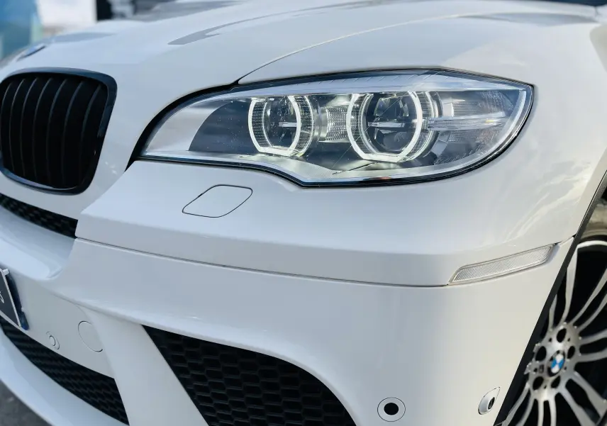Gros plan sur l'avant droit blanc d'un BMW X6 50D M 2013, mettant en valeur le phare bi-xénon et la calandre noire.