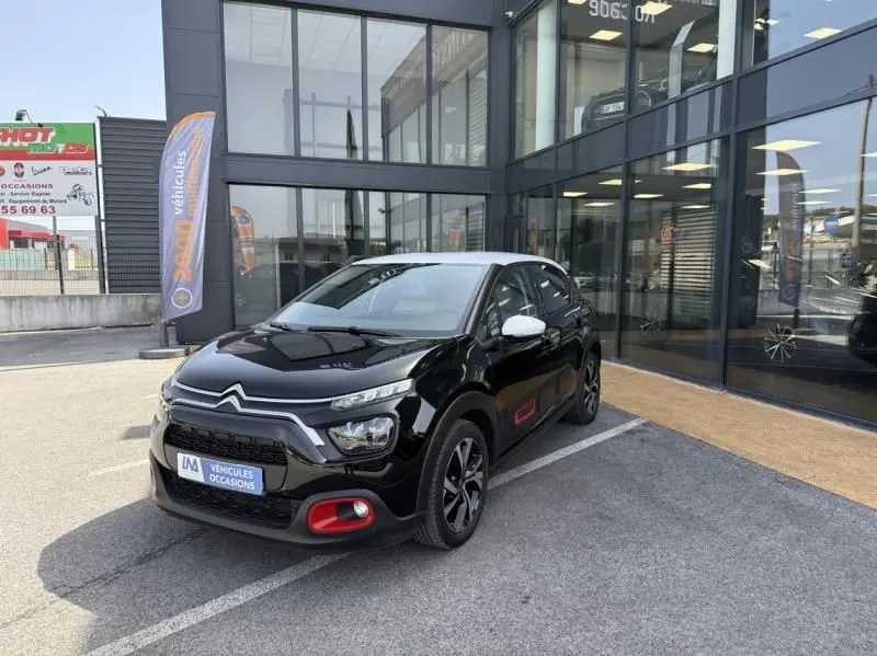 Citroën C3 2021 noir avec toit blanc vue 3/4 avant droit, détails rouges sur pare-chocs et portière, stationnée devant un showroom.