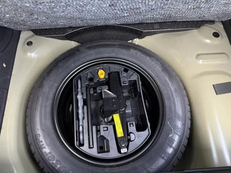 Vue plongeante sur la roue de secours et le kit d'outils dans le coffre d'une Citroën C3 noire toit blanc 2021.