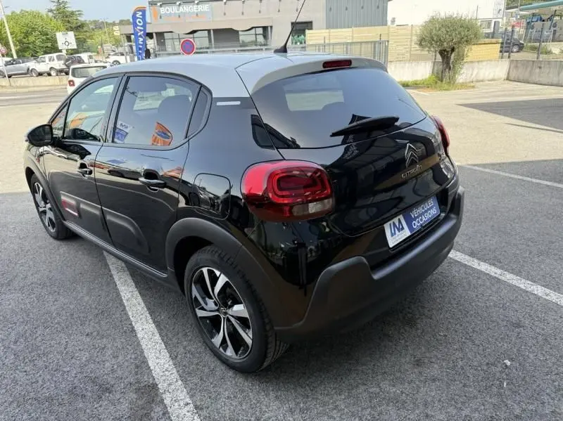 Vue 3/4 arrière droite d'une Citroën C3 noire avec toit blanc, jantes alliage et feux arrière distinctifs, stationnée en extérieur.