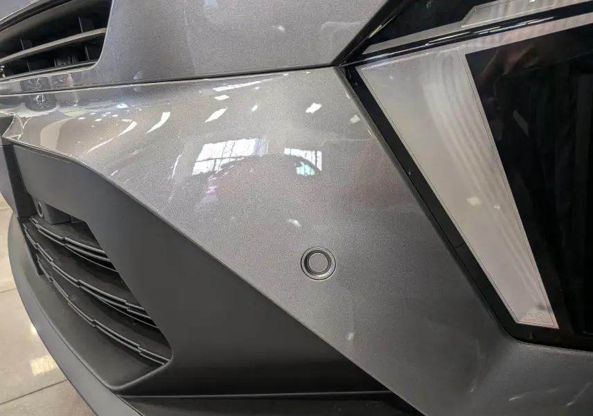 Gros plan sur le pare-chocs avant gris Cassiopé du Renault Symbioz E-Tech, mettant en valeur le capteur de stationnement rond.