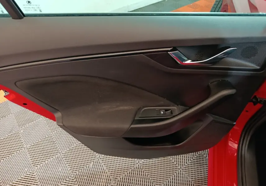 Vue intérieure de la porte avant gauche rouge d'une Skoda Kamiq 2024 avec poignée chromée et commande de vitre électrique.