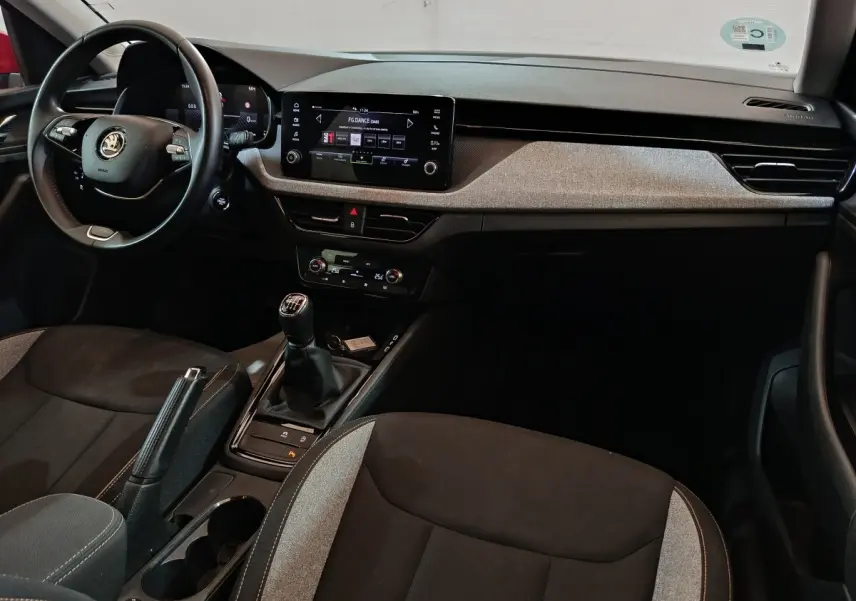 Vue intérieure avant du Skoda Kamiq 2024, volant cuir noir, tableau de bord avec écran tactile central et levier de vitesses manuel.