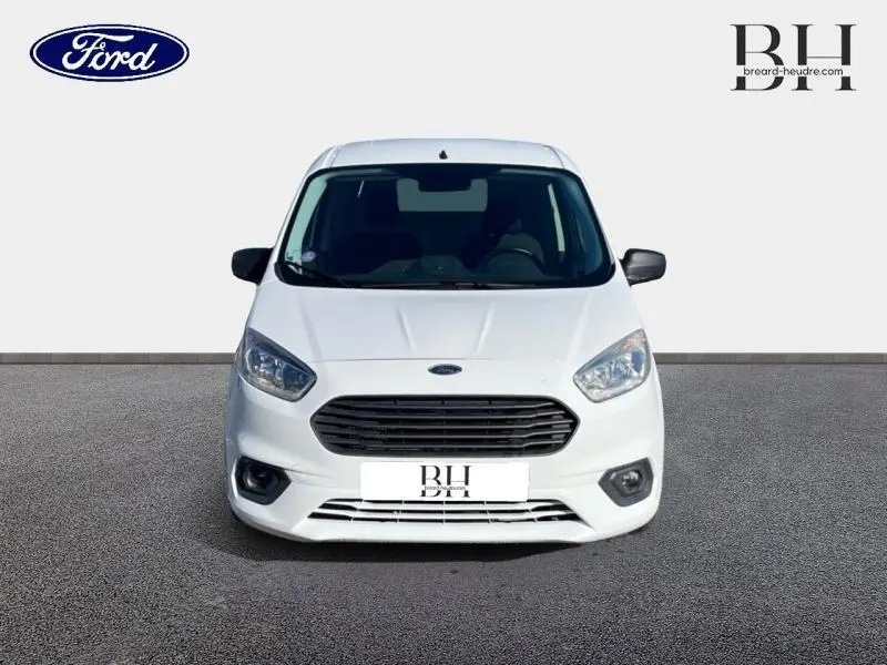 Vue de face du fourgon Ford Transit Courier blanc Glacier avec calandre noire et phares halogènes visibles.