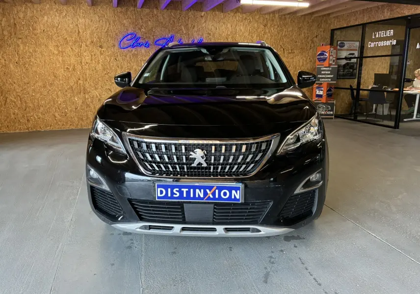 Vue frontale d'un Peugeot 3008 noir 2020 avec calandre chromée et plaque "DISTINXION" en intérieur d'atelier.