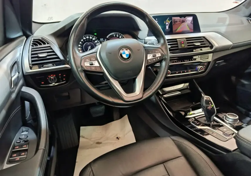 Vue intérieure avant du BMW X3 xDrive30e 2020, volant cuir multifonctions, tableau de bord avec écran de navigation et caméra de recul.