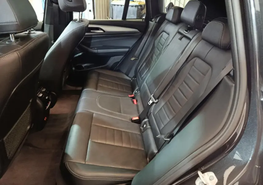Vue intérieure côté droit des sièges arrière en cuir noir du BMW X3 xDrive30e gris foncé, avec ceintures et appuie-têtes visibles.