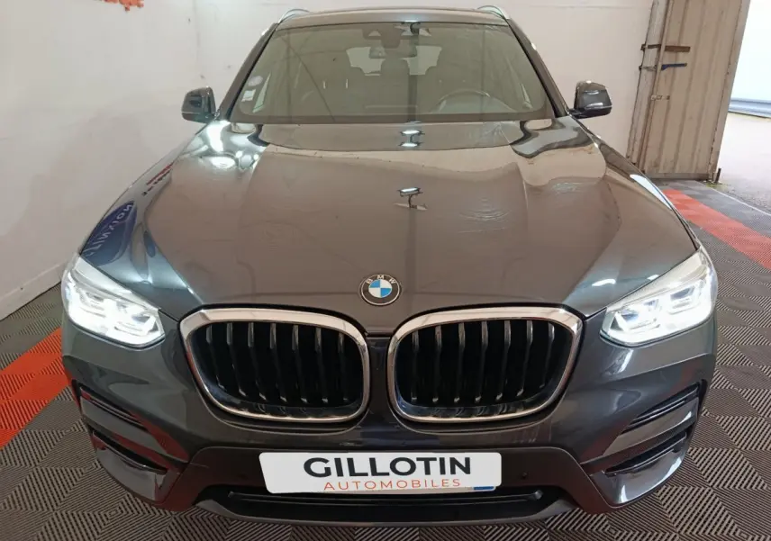 Vue avant d'une BMW X3 xDrive30e gris foncé avec calandre double haricot et phares LED allumés dans un garage.