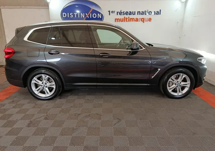 Vue profil côté gauche d’un BMW X3 xDrive30e gris foncé dans un showroom avec logo Distinxion en arrière-plan.