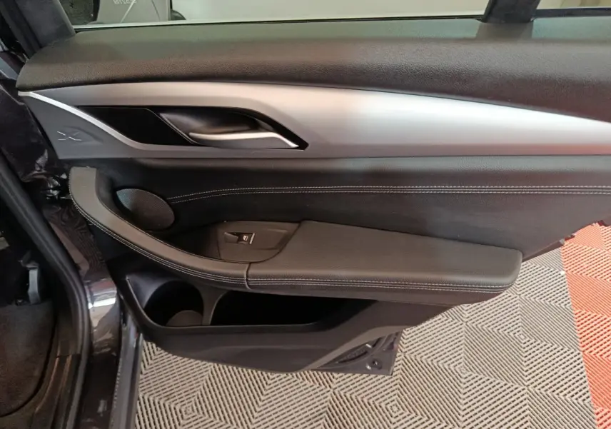 Vue intérieure côté gauche de la porte avant d’une BMW X3 gris foncé avec garniture noire et insert argenté.