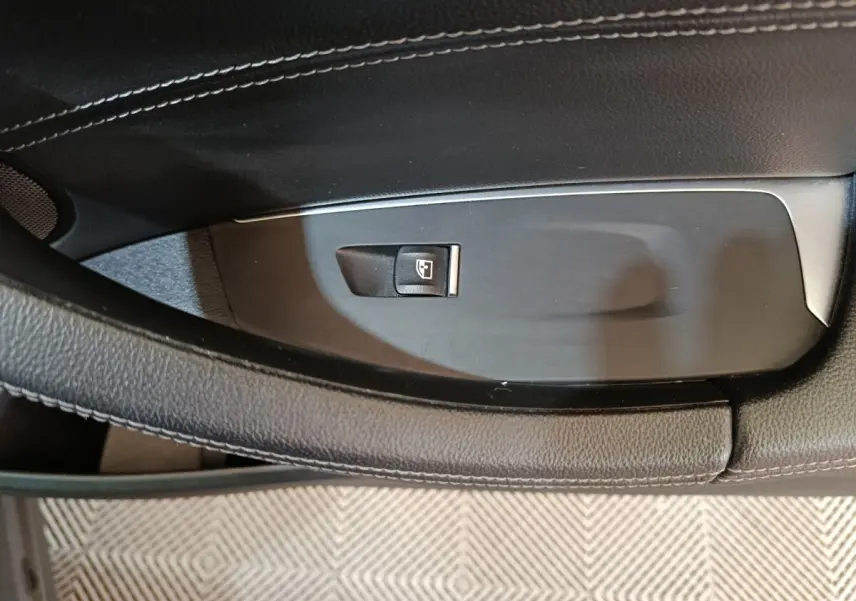 Gros plan sur le bouton de commande de lève-vitre côté gauche dans l’intérieur noir et gris foncé d’une BMW X3 xDrive30e.