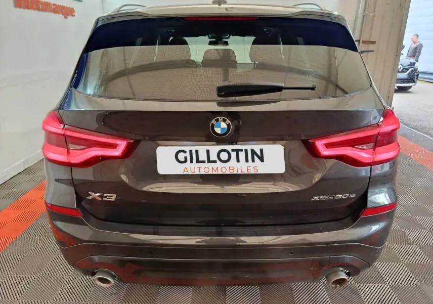 Vue arrière d’un BMW X3 xDrive30e gris foncé avec feux LED allumés et double sortie d’échappement visible.