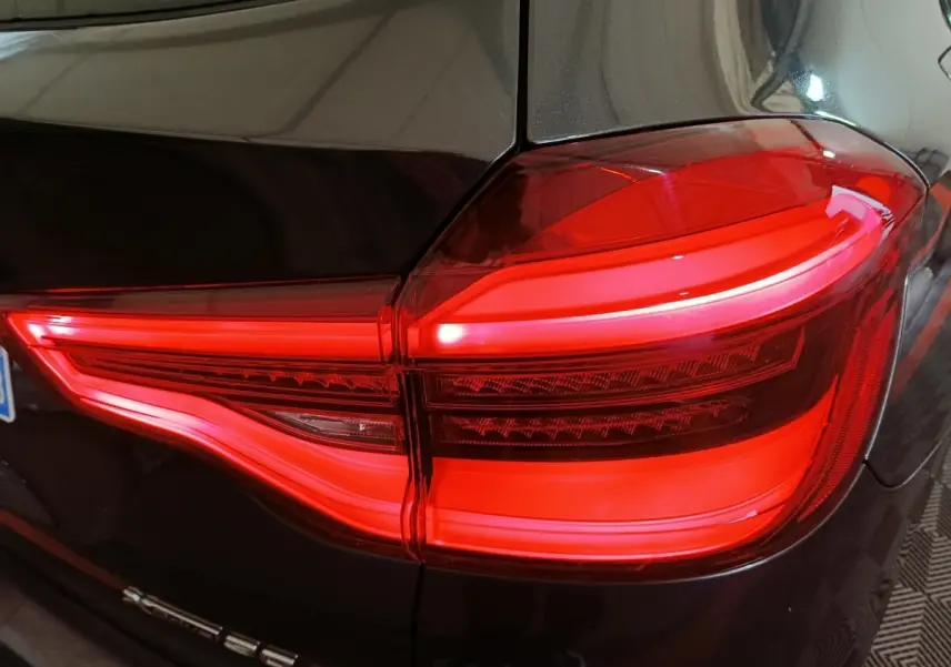 Gros plan sur le feu arrière droit allumé d’un BMW X3 xDrive30e gris foncé, soulignant son design lumineux distinctif.